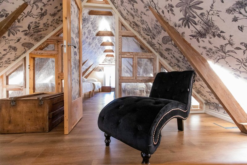 Attic room under sloped beams covered in black-and-white botanical wallpaper, with a black velvet chaise longue