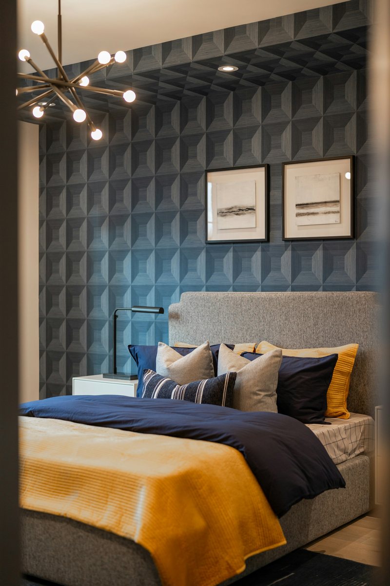 Bedroom with navy three-dimensional textured wallpaper, a brass sputnik chandelier and a bed with mustard throw