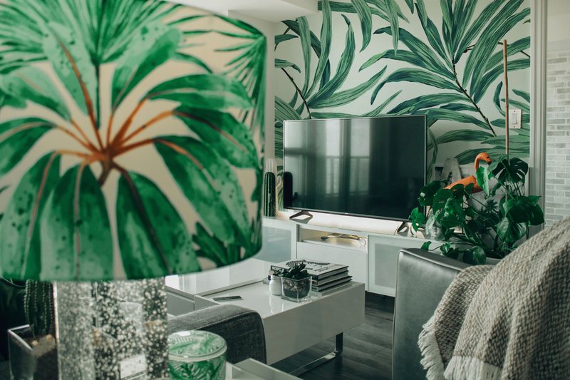 Living room with large green palm-leaf wallpaper behind a white media console, with a matching palm-print lampshade in front