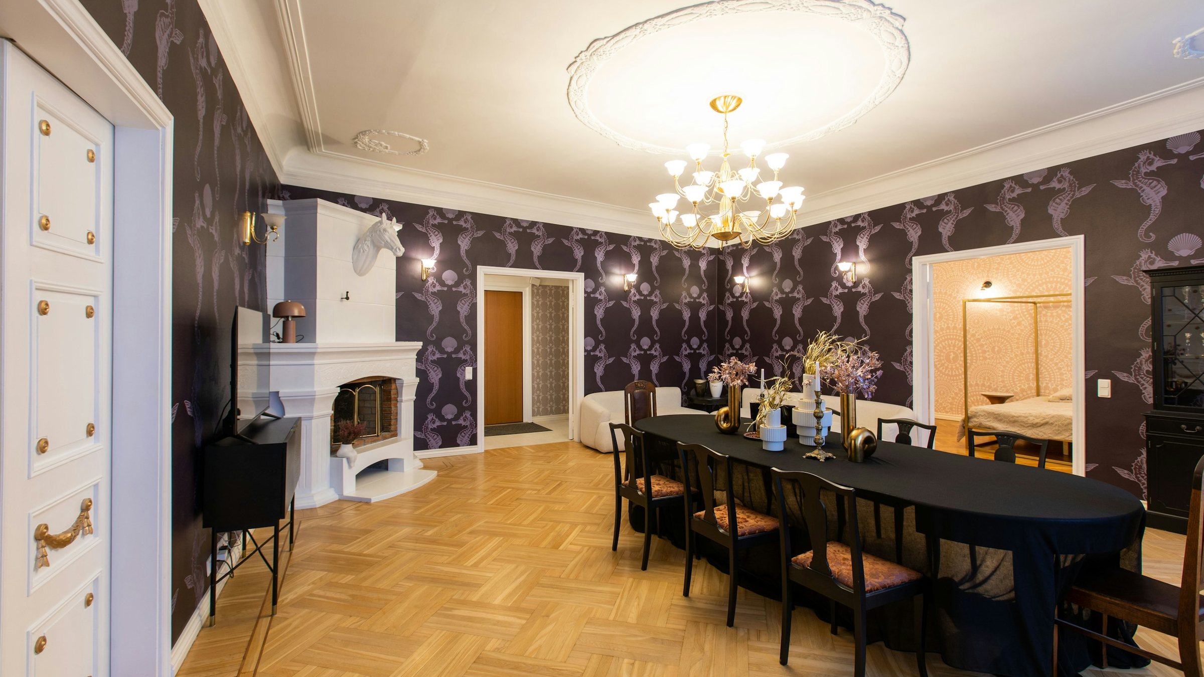 Dining room with dark botanical wallpaper, a crystal chandelier, a white fireplace and a long dining table
